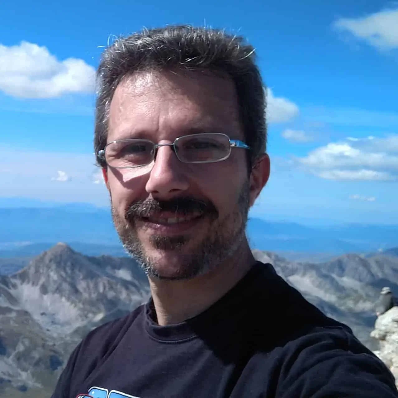 Michele sonriendo con muchos picos de montañas en el fondo.